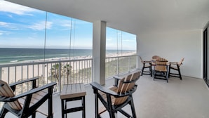 Ein Balkon mit Blick auf den Strand und das Meer. Holzstühle und ein Tisch sind vorhanden.