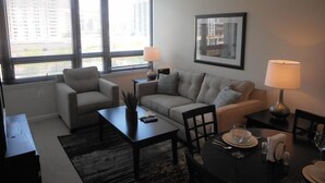 A modern living room with a sofa, armchairs, a coffee table, and a dining table set for two. - National at Reston Town Center (Reston)