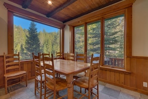Enjoy meals in this dining area with a view of the surrounding forest, surrounded by large windows and wooden paneling.