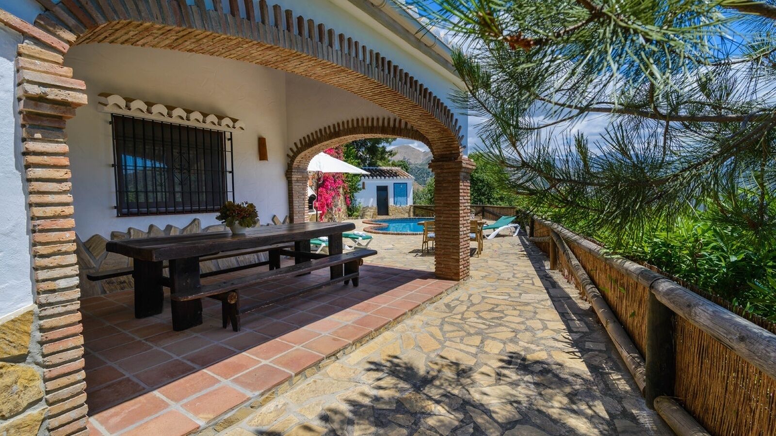 Ein überdachter Sitzbereich mit Pool im Hintergrund.