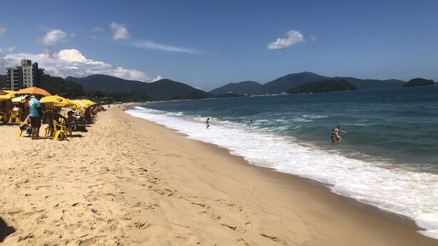 A beach with yellow umbrellas, people sunbathing, and a view of the sea and mountains.