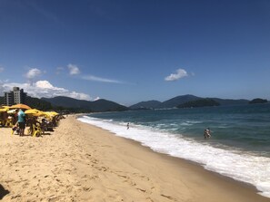 A beach with yellow umbrellas, people sunbathing, and a view of the sea and mountains.