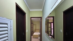 A narrow hallway with doors on both sides, leading to a bedroom with a bed and a dresser.
