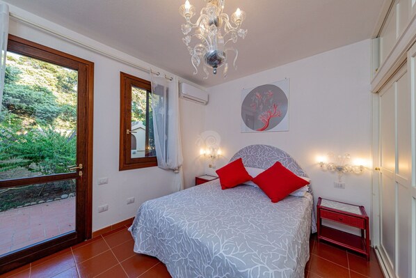 A bedroom with a bed, a chandelier, a window, and a painting on the wall.