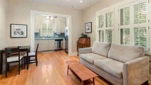 A living room with a sofa, a wooden coffee table, and a dining area with a table and chairs. There is a kitchen in the background with a refrigerator and cabinets. - Hyde Park Historic District - Close To Everything Austin Has To Offer! (Austin)