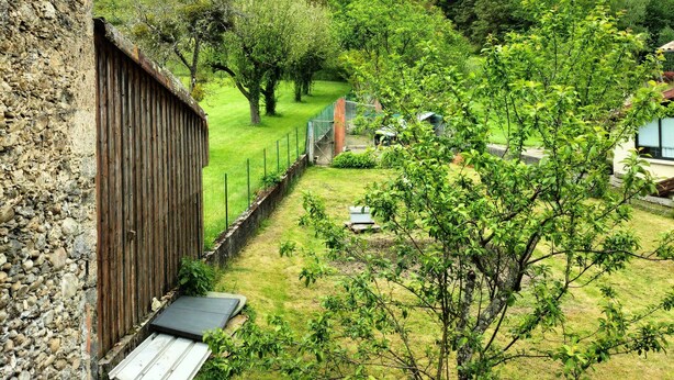 A stone building with a wooden fence and a view of a green landscape with trees and a hill in the background. - The caminada, house in the heart of the Pyrenees Ariégeoises (Fougax-et-Barrineuf)