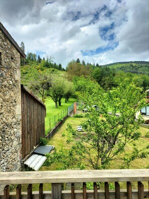 Un edificio in pietra con una recinzione in legno e vista su un paesaggio verde con alberi e una collina sullo sfondo.
