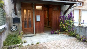 A building entrance with a wooden door, a metal gate, and a small garden with purple flowers. - The caminada, house in the heart of the Pyrenees Ariégeoises (Fougax-et-Barrineuf)