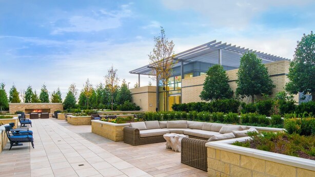 A modern outdoor patio area with a fire pit, seating arrangements, and a glass-enclosed building. - National Tysons Corner (McLean)