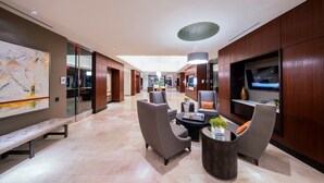 A spacious lobby with a long bench, seating area, and a TV screen displaying news. - National Tysons Corner (McLean)