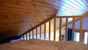 Une chambre avec un plafond en pente, des poutres en bois, un lit et une fenêtre.