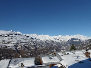 Un pueblo de montaña con tejados nevados y una vista despejada de picos nevados en la distancia.