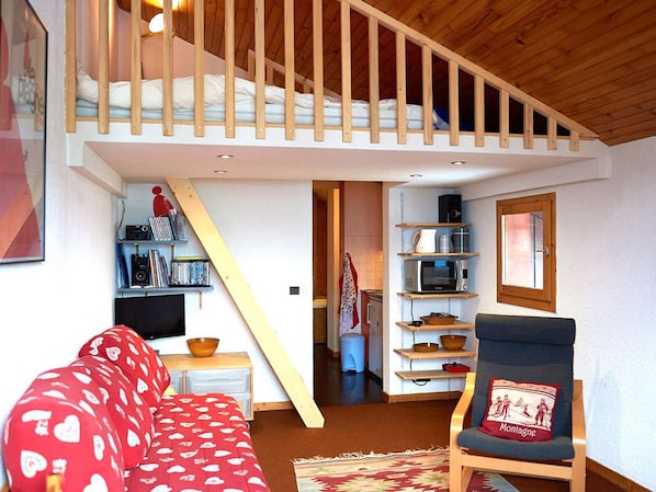Una sala de estar acogedora con un sofá rojo, una silla de madera y una escalera que sube a una habitación superior.