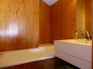 Un baño con paredes de madera, una bañera blanca y un lavamanos con dos botellas de líquido.