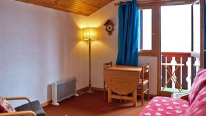 Une pièce chaleureuse avec un plafond en pente, une table et des chaises en bois, une lampe sur pied, un radiateur et une fenêtre ornée de rideaux bleus.