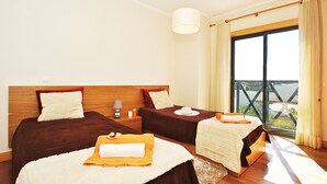 A hotel room with two beds, a large window with curtains, a wooden headboard, and a view of the outside. - Villa w/ BBQ & pool near the Strip, Albufeira (Albufeira)