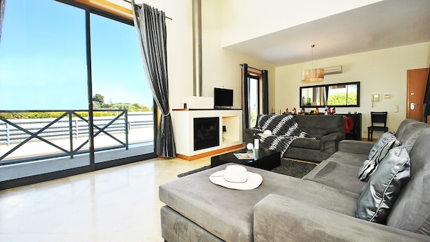 A modern living room with a large grey sofa, a small white table with a hat, and a TV on a black stand. - Villa w/ BBQ & pool near the Strip, Albufeira (Albufeira)