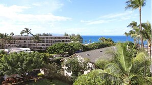 A hotel with a view of the ocean, surrounded by palm trees and greenery. - Kihei Akahi Resort, ocean view, steps from the beach (Kihei)