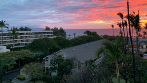 A coastal view with a sunset, palm trees, and a building complex. - Kihei Akahi Resort, ocean view, steps from the beach (Kihei)