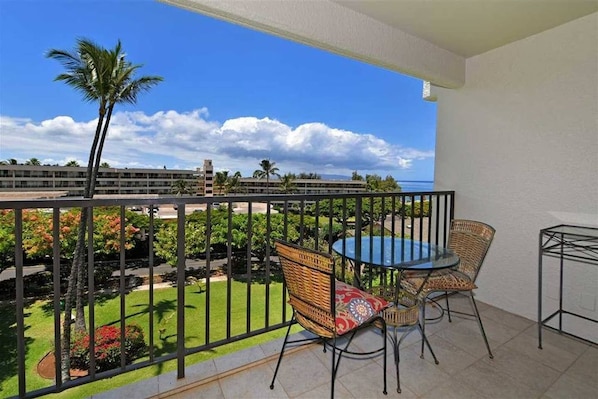 Enjoy a serene view of the lush garden from this balcony, featuring a round table and two comfortable chairs.