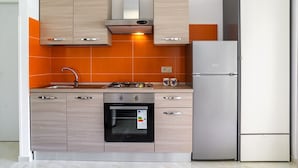 A modern kitchen with wooden cabinets, a gas stove, an oven, and a refrigerator. - Soleil Suite in Giardini Naxos (Giardini Naxos)