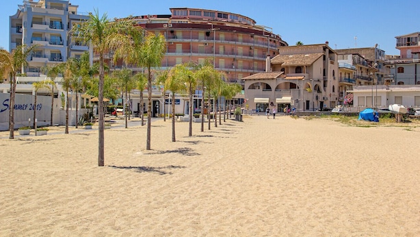 A beachfront hotel with multiple floors, palm trees, and a sandy beach. - Soleil Suite in Giardini Naxos (Giardini Naxos)