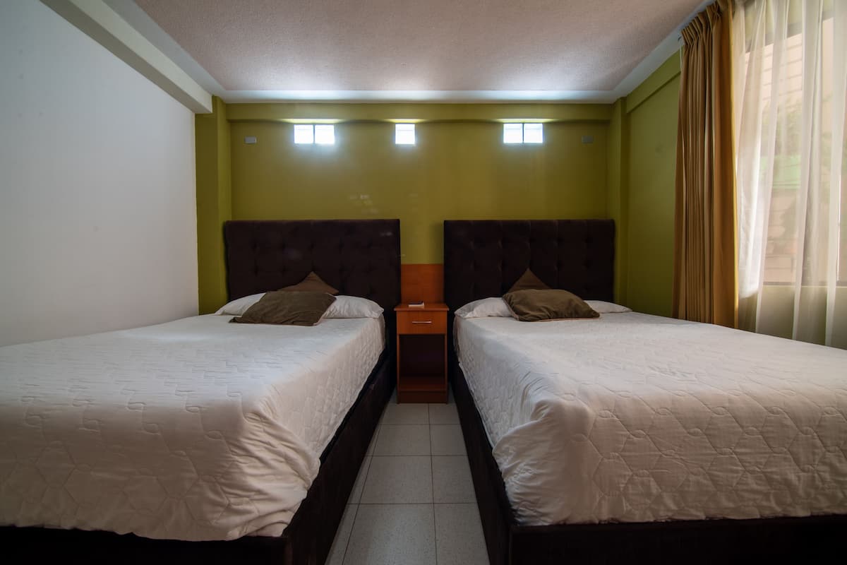 Una habitación con dos camas, una mesita de noche pequeña y una ventana con cortinas.