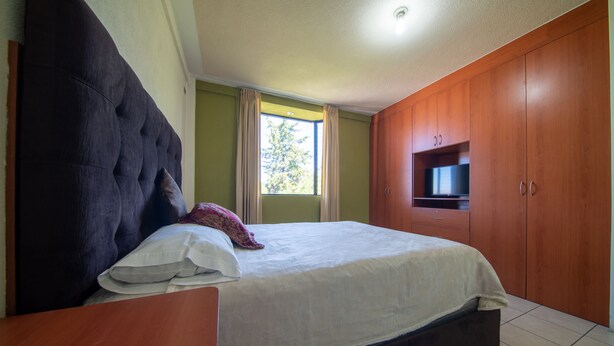 A bedroom with a large bed, wooden wardrobe, and a television on the wall. - Hotel de Santa Maria (Santa Cruz del Quiché)