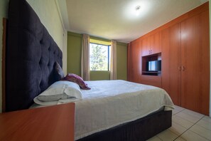 A bedroom with a large bed, wooden wardrobe, and a television on the wall. - Hotel de Santa Maria (Santa Cruz del Quiché)