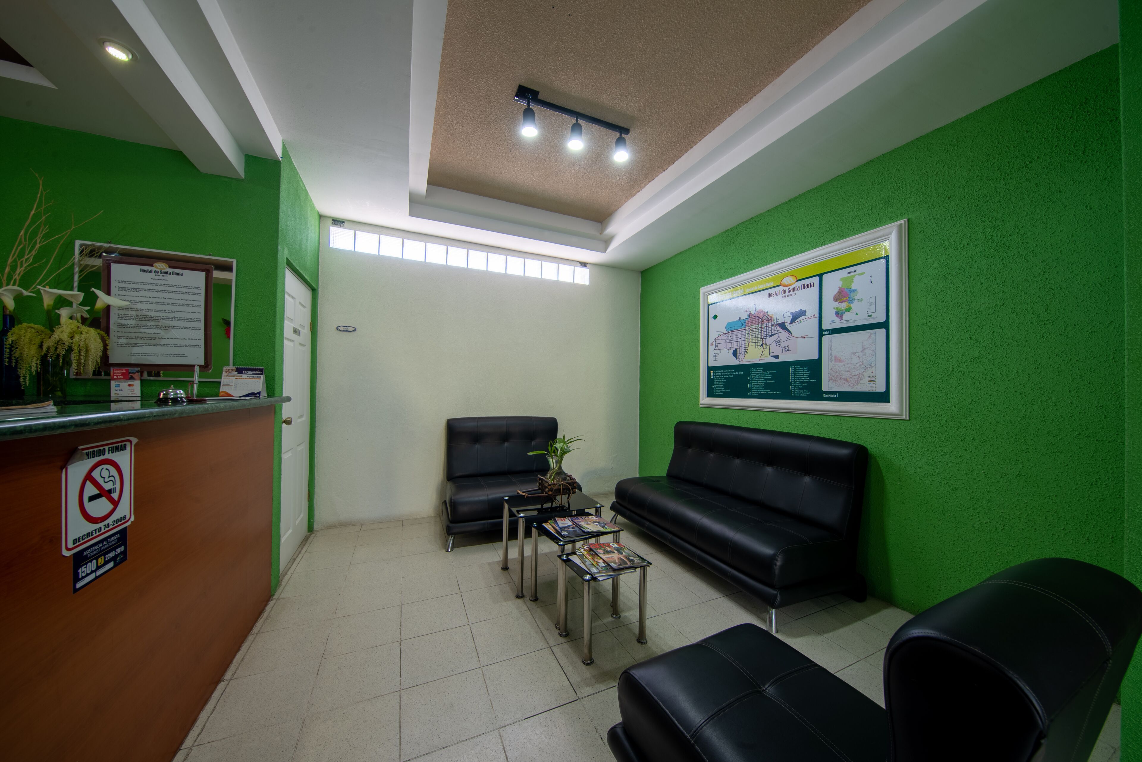 A reception area with a green wall, a reception desk, two black leather sofas, and a small coffee table.