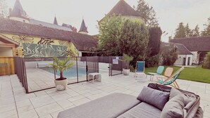 Um pátio com piscina, cadeiras de descanso e área de estar coberta.