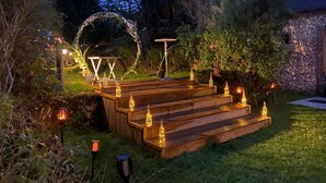 Um deck de madeira ao ar livre com escadas, cercado por vegetação e muros de pedra.