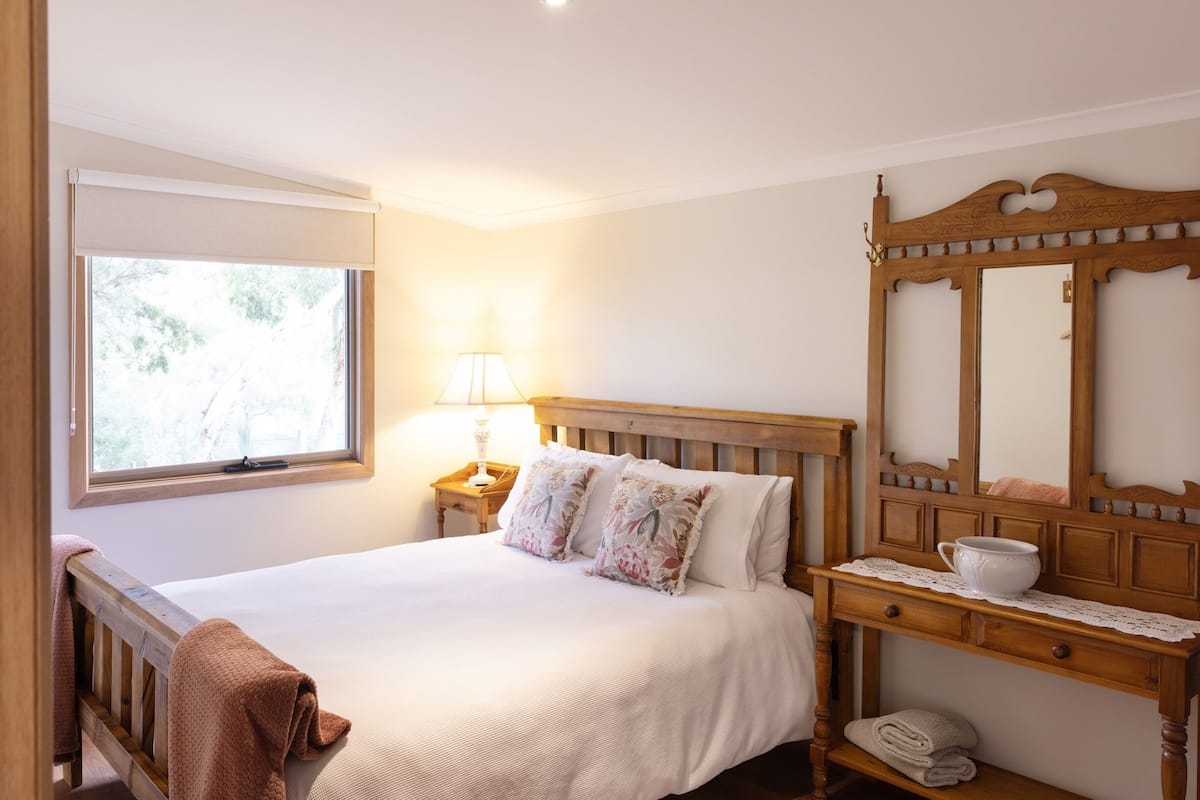 A bedroom with a bed, a bedside table with a lamp, a wooden dresser, and a large mirror.