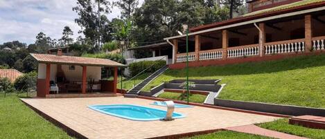 A pool area with a small building, a covered patio, and a staircase leading up a hill.