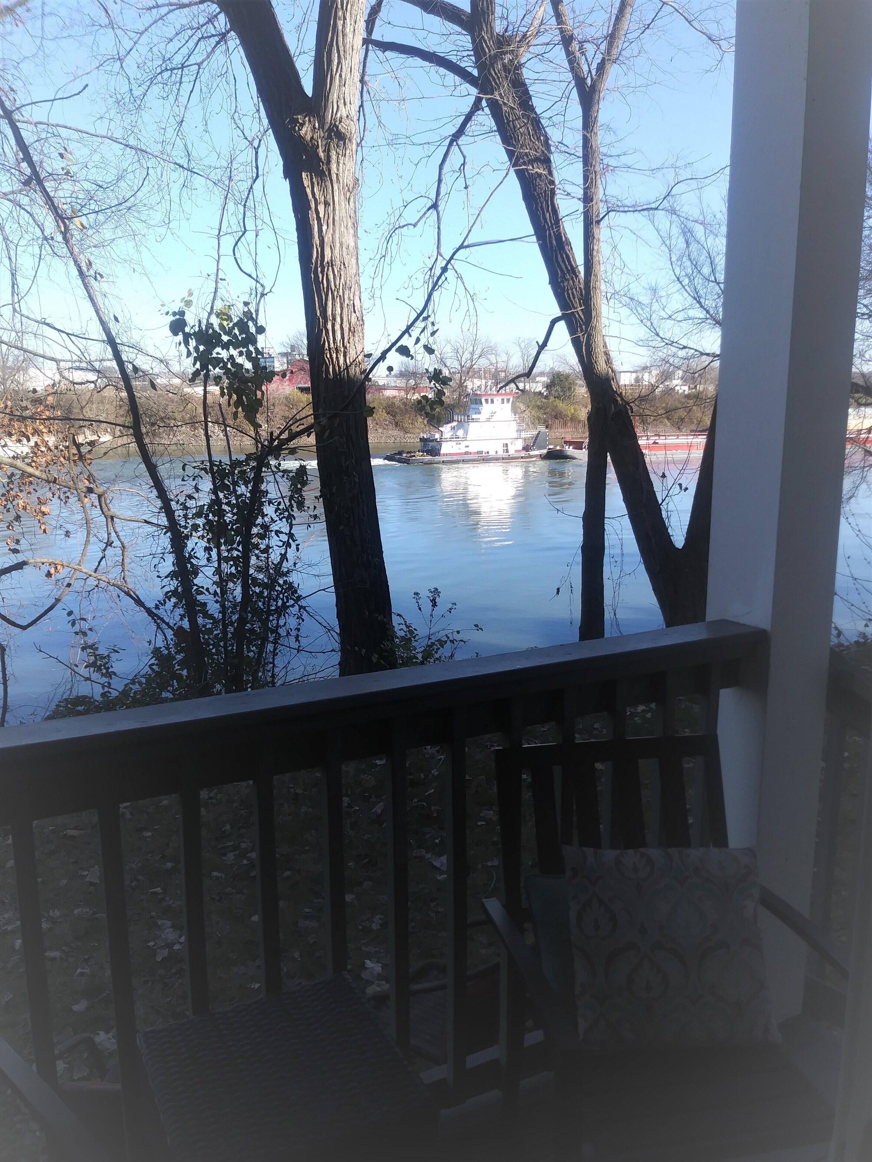 A view from a covered porch overlooking a river with a boat docked on the opposite bank.