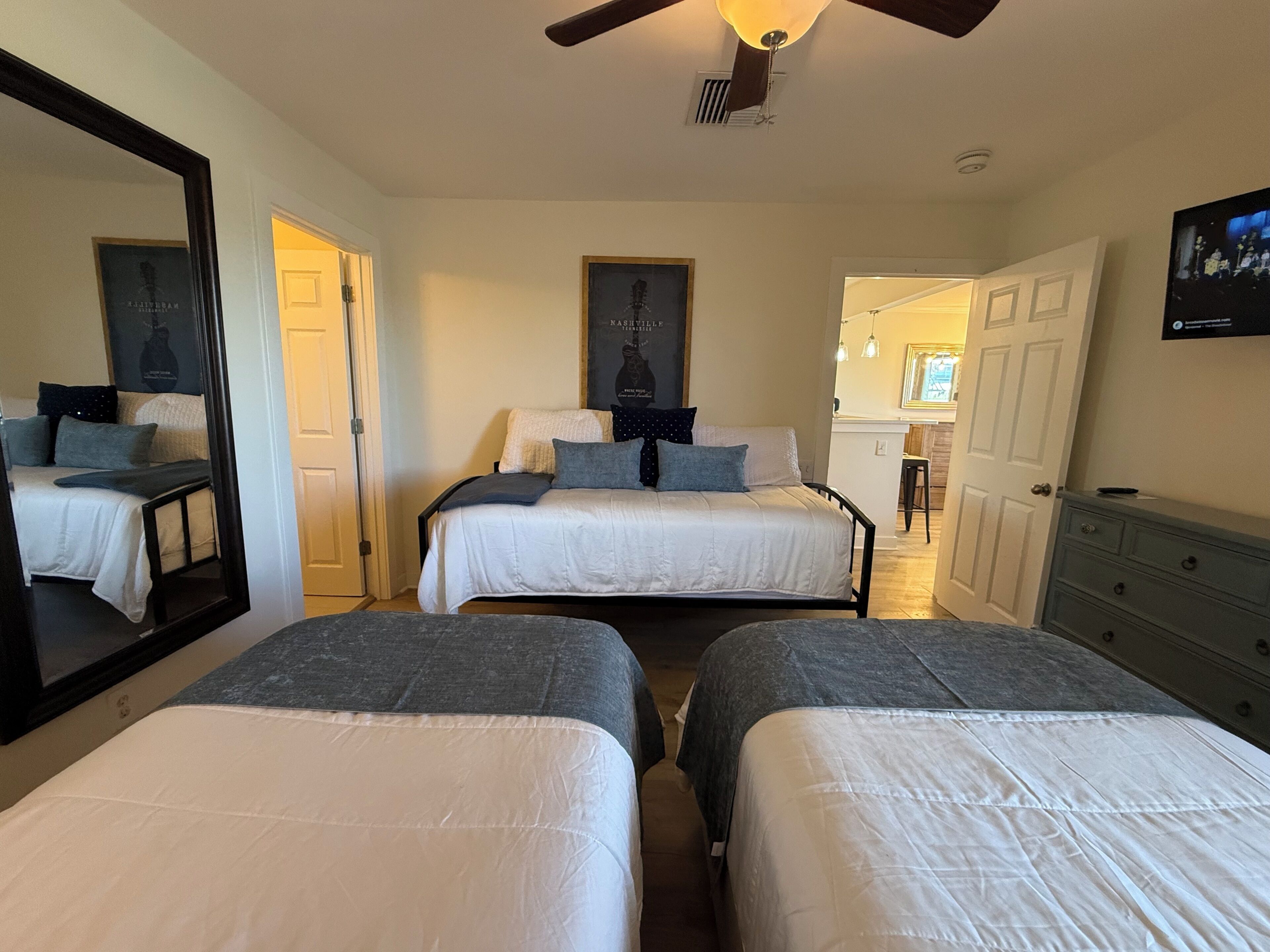 A bedroom with two beds, a large mirror, a ceiling fan, and a TV.