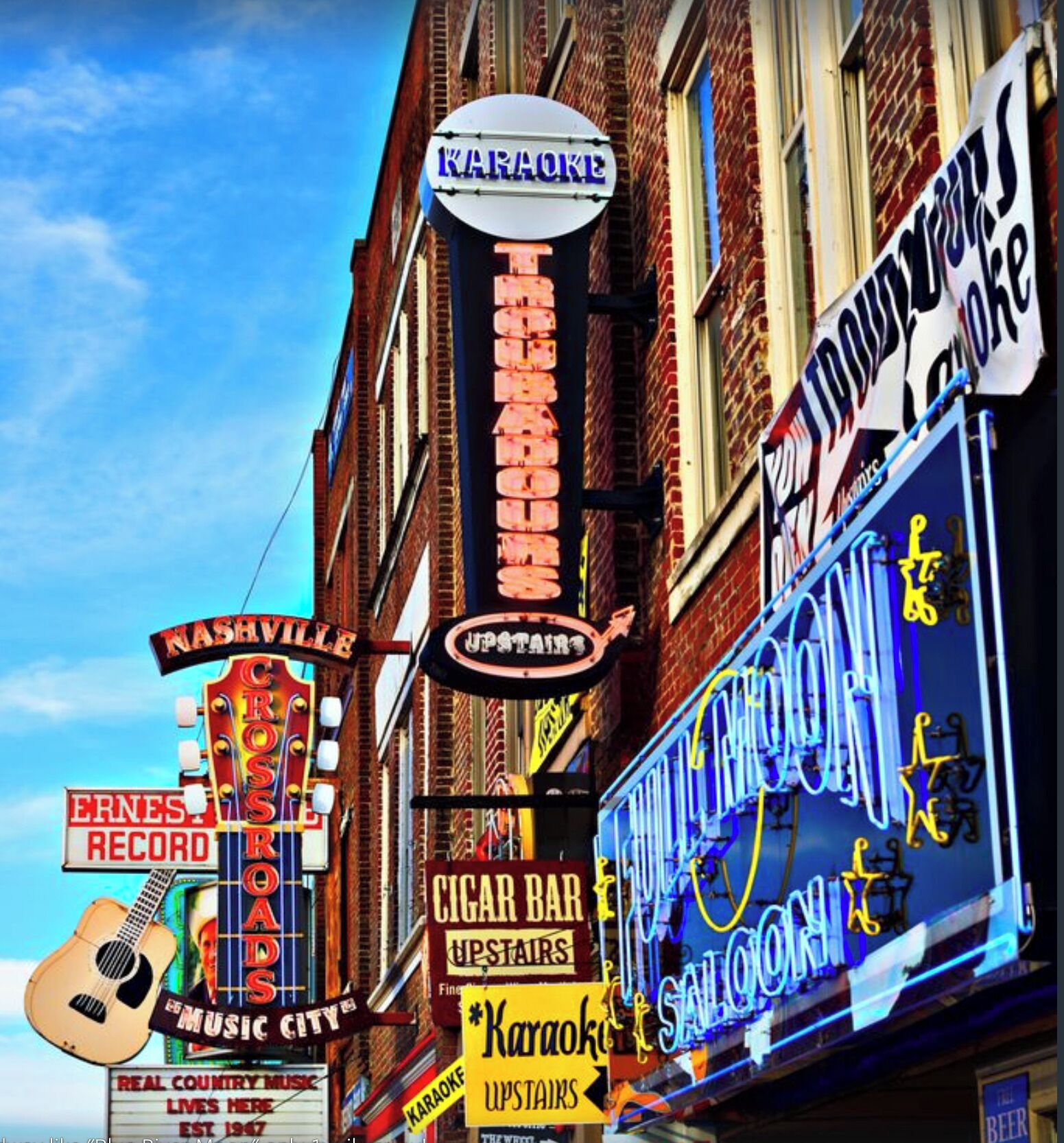A building with multiple signs, including a karaoke sign, a cigar bar, and a music city sign.