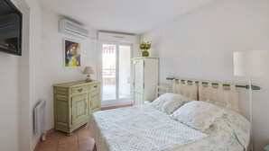 A bedroom with a bed, a dresser, an air conditioner, a radiator, and a door leading to an outdoor area. - Appartement Lanterne – Welkeys (Nice)