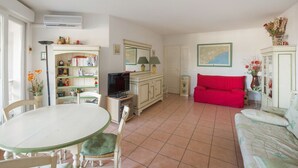 A living room with a dining table, red sofa, and a television. - Appartement Lanterne – Welkeys (Nice)