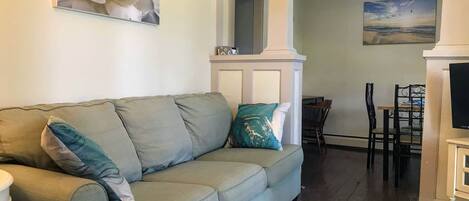 A living room with a light blue sofa, a star-patterned rug, a ceiling fan, and a painting of a beach scene.