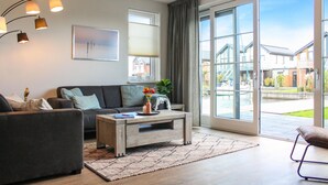 A modern living room with a sofa, coffee table, and a large window offering a view of a residential area.