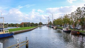 A canal with boats docked on both sides, a grassy area, and buildings in the background.
