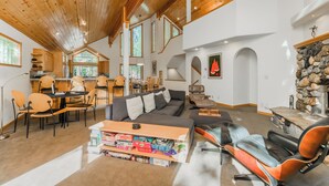 A spacious living area with a wooden ceiling, a fireplace, and a dining area with chairs and a table. - Star Pine_Luxury w/Game Room, Pool Table & HOA Amenities (Hot Tub/Sauna/Gym) (Truckee)