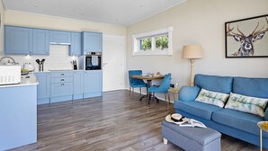 A compact living space with a kitchenette, a dining area, and a seating area with a sofa and ottoman. - Rafters -  a lodge that sleeps 2 guests  in 1 bedroom (Georgeham)
