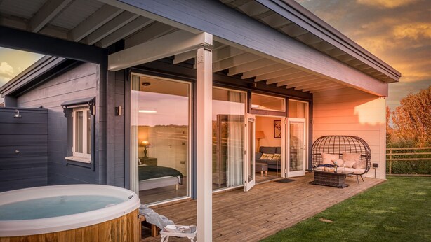 A modern house with a hot tub, a covered patio, and a glass door leading to a bedroom. - Rafters -  a lodge that sleeps 2 guests  in 1 bedroom (Georgeham)