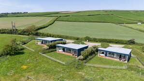 A modern farmhouse with three blue-roofed buildings, each with a patio and large windows. - Rafters -  a lodge that sleeps 2 guests  in 1 bedroom (Georgeham)