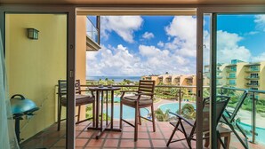 Een balkon met uitzicht op een zwembad en resortgebouwen, met een tafel en stoelen.