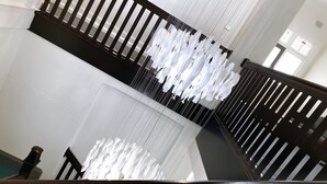 Un escalier avec une rampe, un luminaire suspendu et une vue sur une pièce avec une fenêtre.