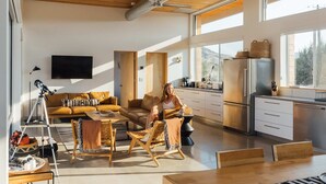 A modern living room with a sofa, chairs, a dining table, and a kitchen area with a refrigerator and cabinets. - Hawk & Mesa By Homestead Modern (Pioneertown)