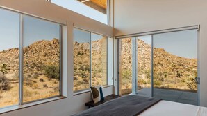 A bedroom with large windows offering a view of a rocky desert landscape. - Hawk & Mesa By Homestead Modern (Pioneertown)